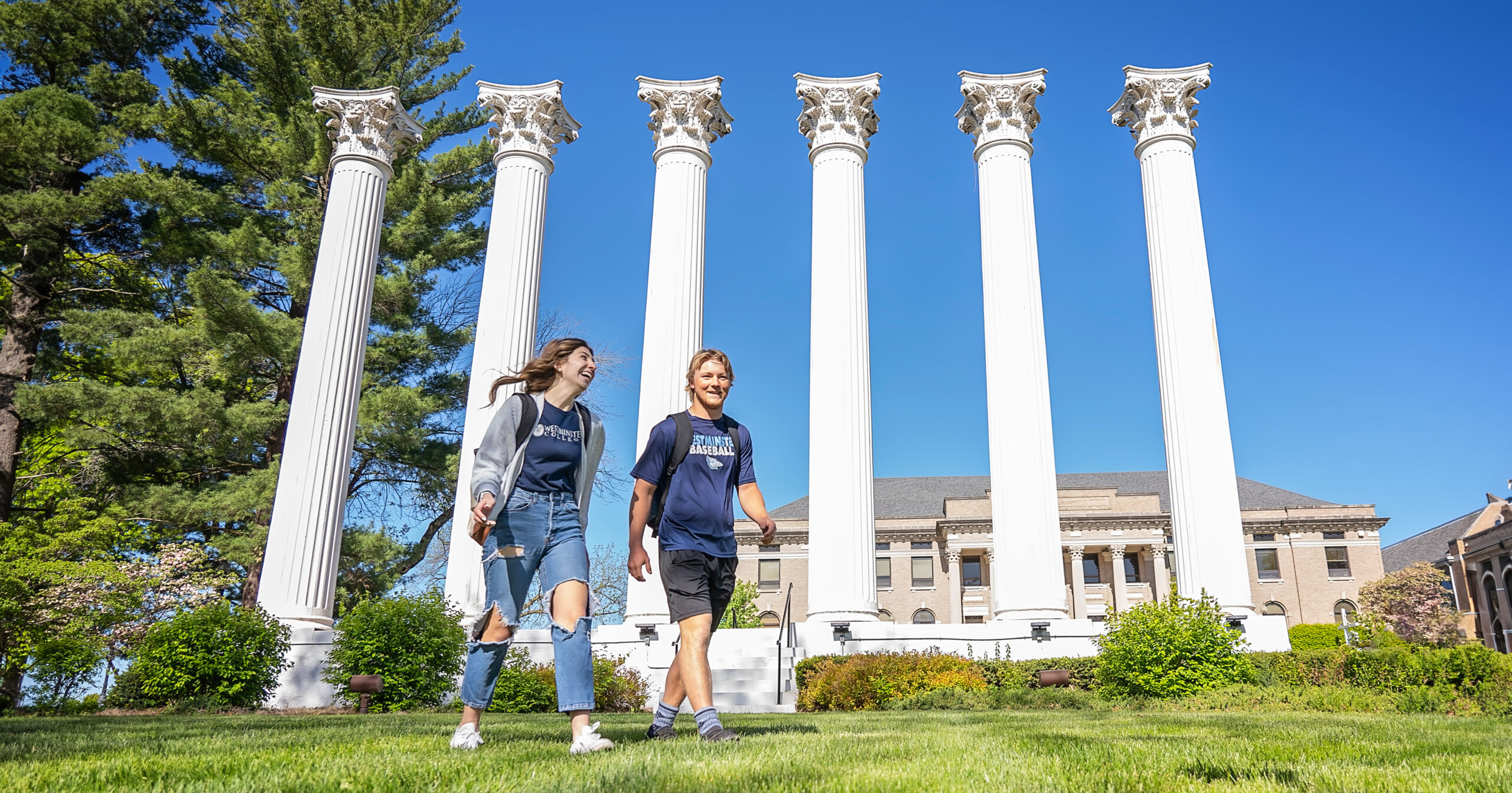 Two students walk together on a sunny day in front of the Columns at Westminster College.