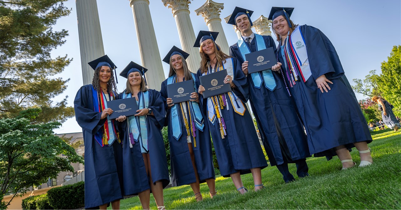 Graduates in blue caps and gowns before the Columns