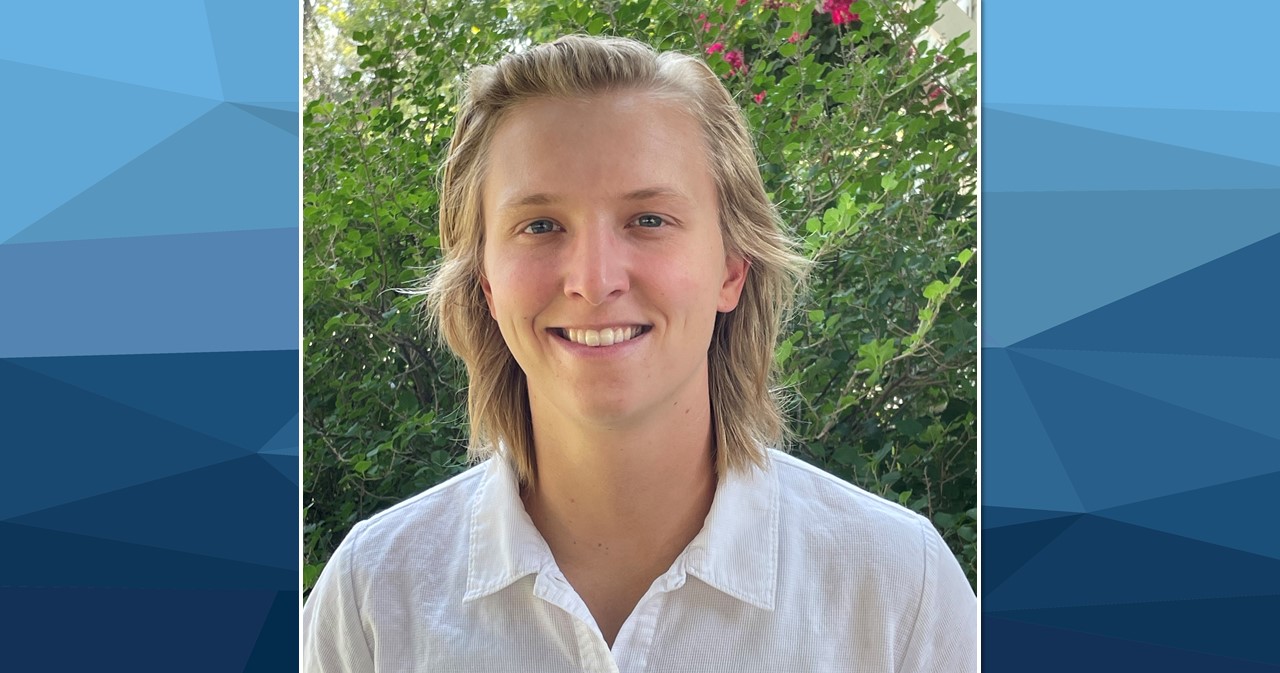 Payton Beeler smiles in front of green foliage on a sunny day wearing a bright white shirt with a collar.
