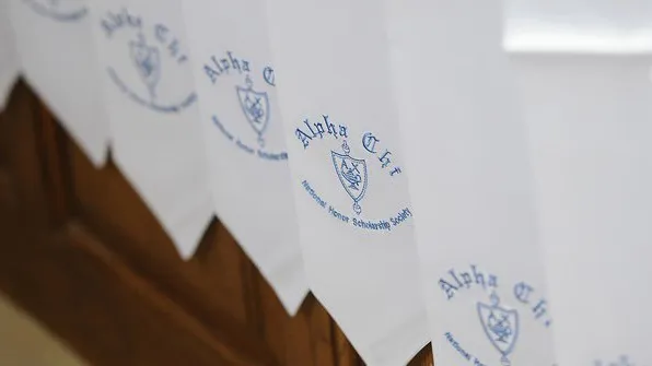 White honor stoles with blue Alpha Chi logos are pictured on a brown table.