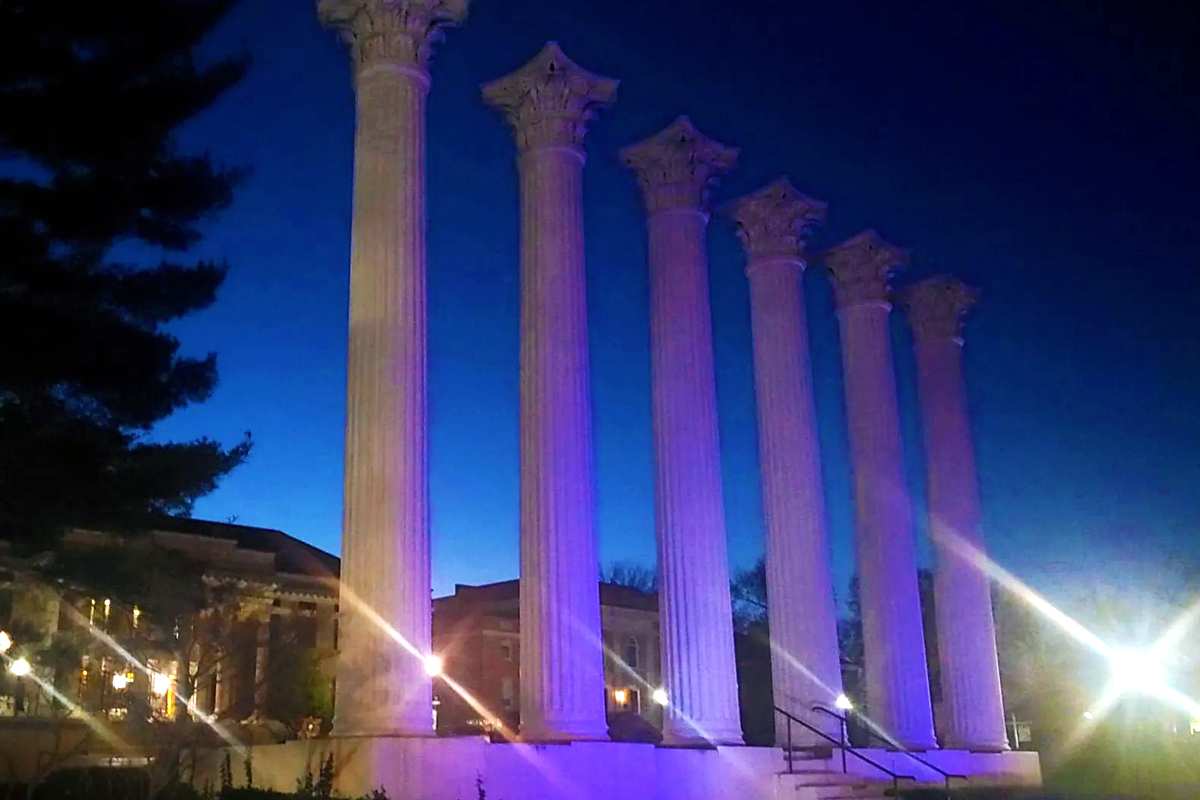 Westminster's Greek revivial columns are pictured at night, with bright lights shades of blue shining on them.