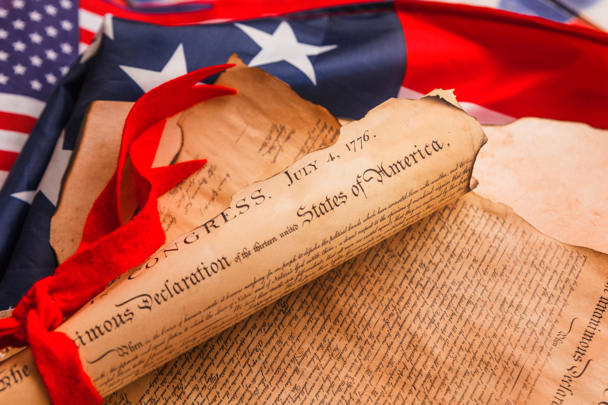 The Declaration of Independence is pictured half rolled up and placed upon an American flag.