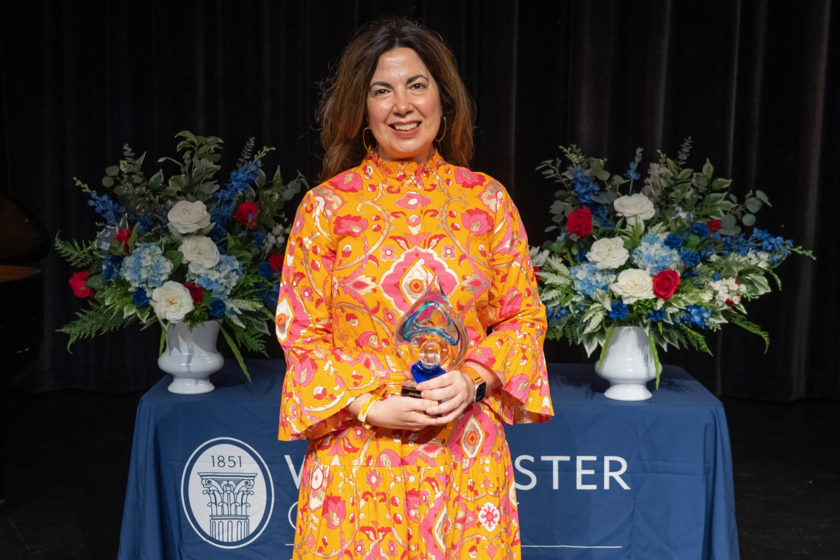 Dr. Natasia Sexton is featured in an orange dress holding an award and standing in front of a table with a navy Westminster College tablecloth.