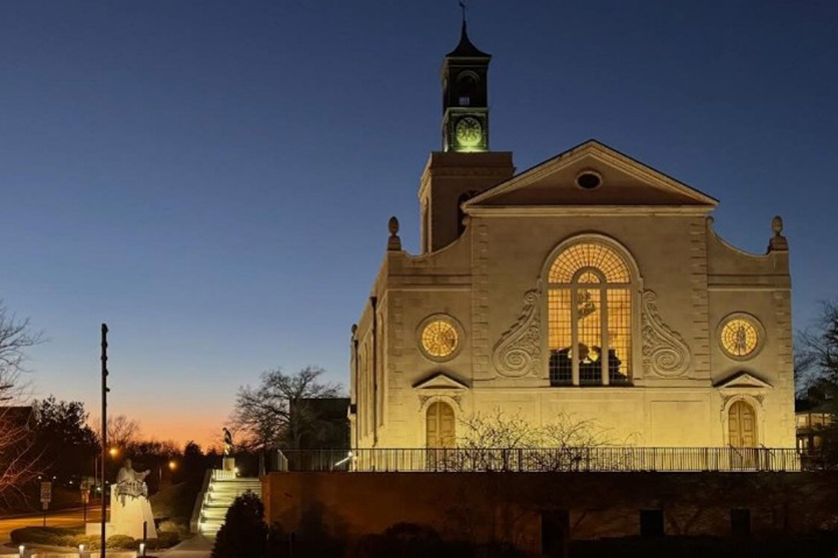 The north side of America's National Churchill Museum is pictured at night, lit up with golden lights. St. Mary the Virgin, Aldermanbury, the Museum's centerpiece, is prominently featured.