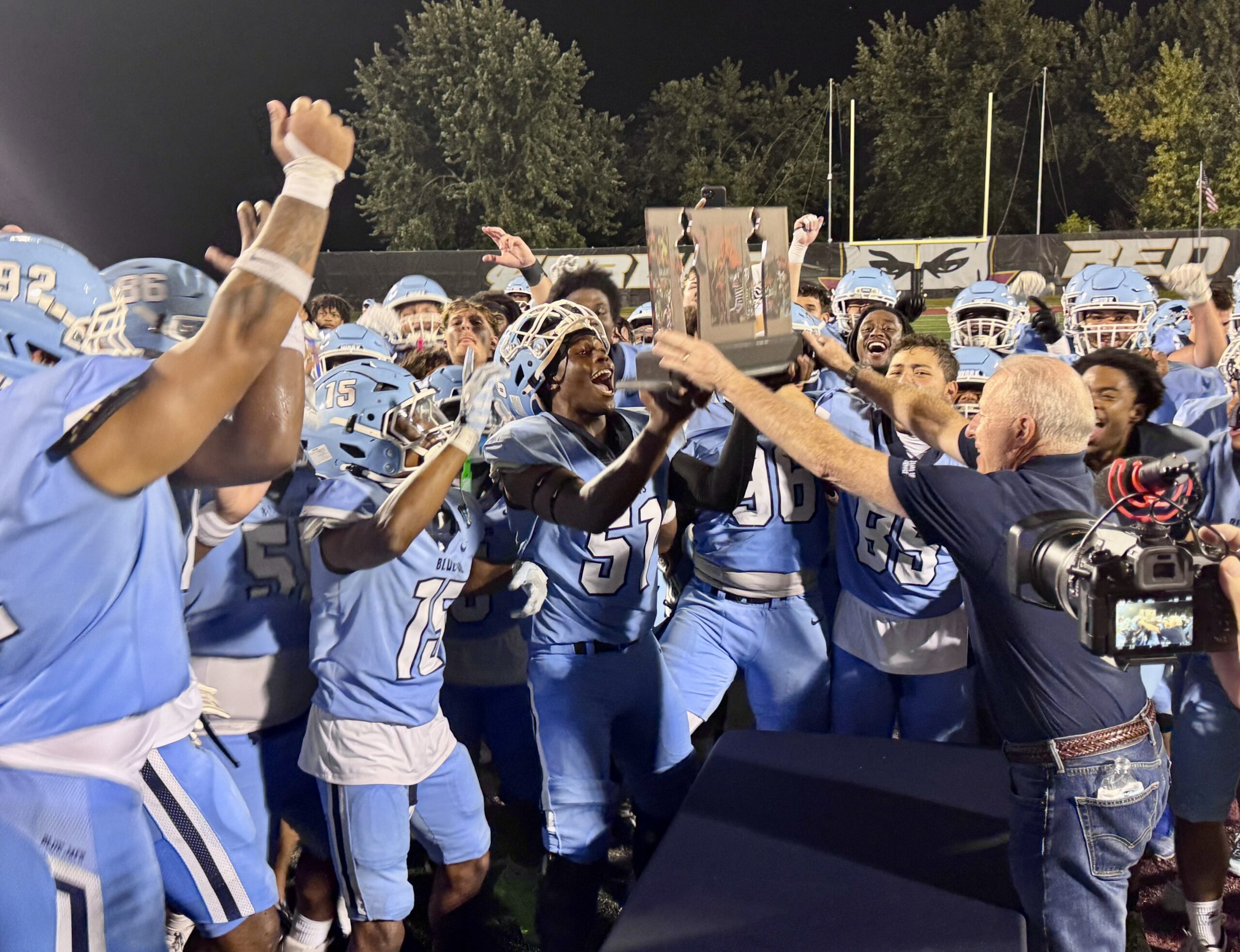 The Blue Jays football team cheers as President Don Lofe hands them the Berlin Wall Bowl trophy at the Red Devils stadium in Eureka.