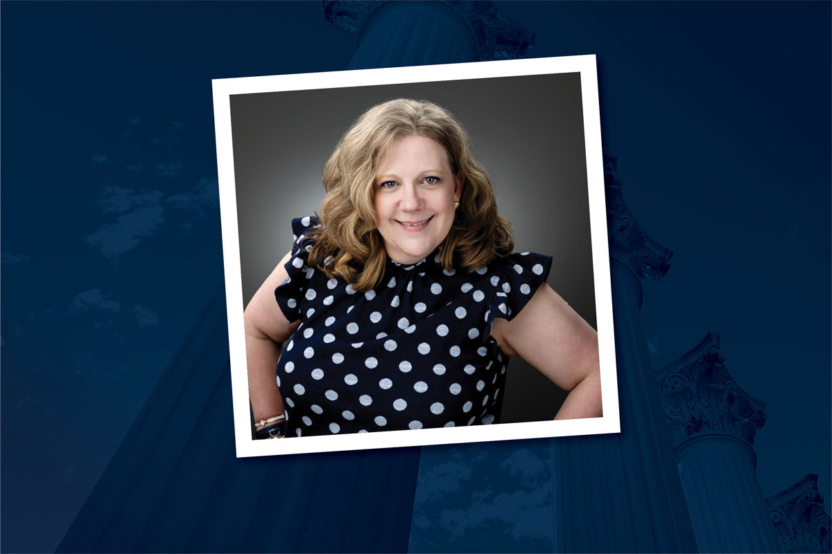 Heather Stewart is pictured wearing a navy blouse with white polka dots, hands on hips, and smiling. Her image is within a square outlined in white that is placed over a rectangular navy background.